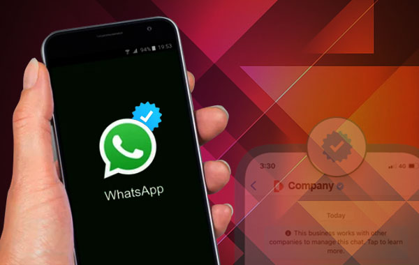 Hand holding smartphone with WhatsApp Business logo and blue tick on screen, abstract geometric background